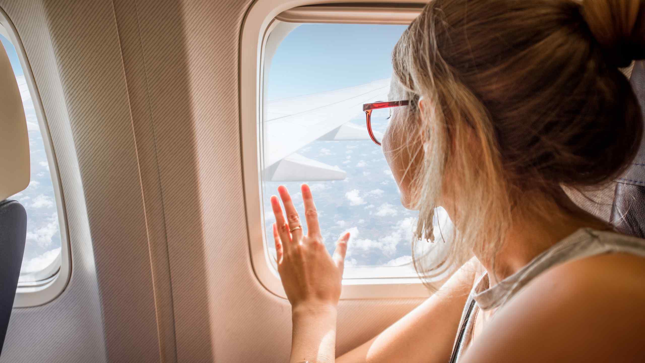 Mujer relajada mirando por la ventanilla de un avión durante su viaje en la betaespera de una transferencia embrionaria.